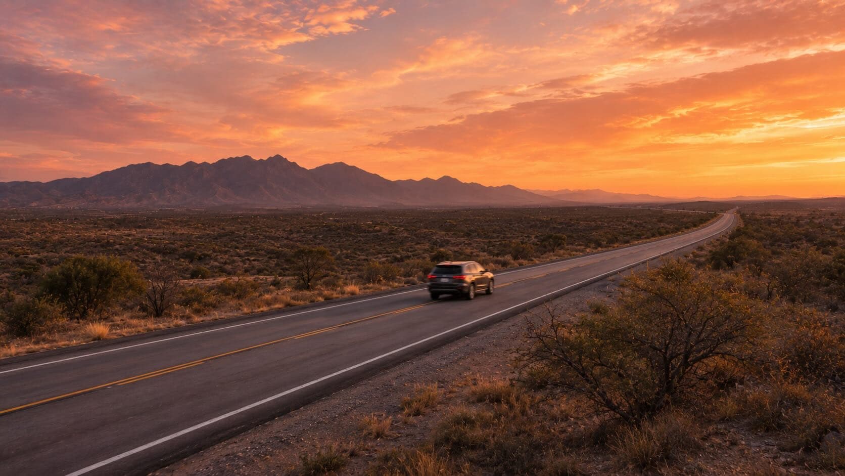 Carretera mexicana abierta al atardecer con coche en movimiento y montañas en el horizonte